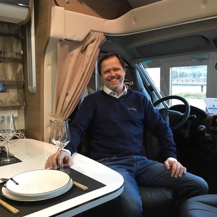 I bildet ser vi Jan Henning Løviknes som smiler mot kamera. Han sitter i butikken til daglig og rådgir de som ønsker å kjøpe bobil.
