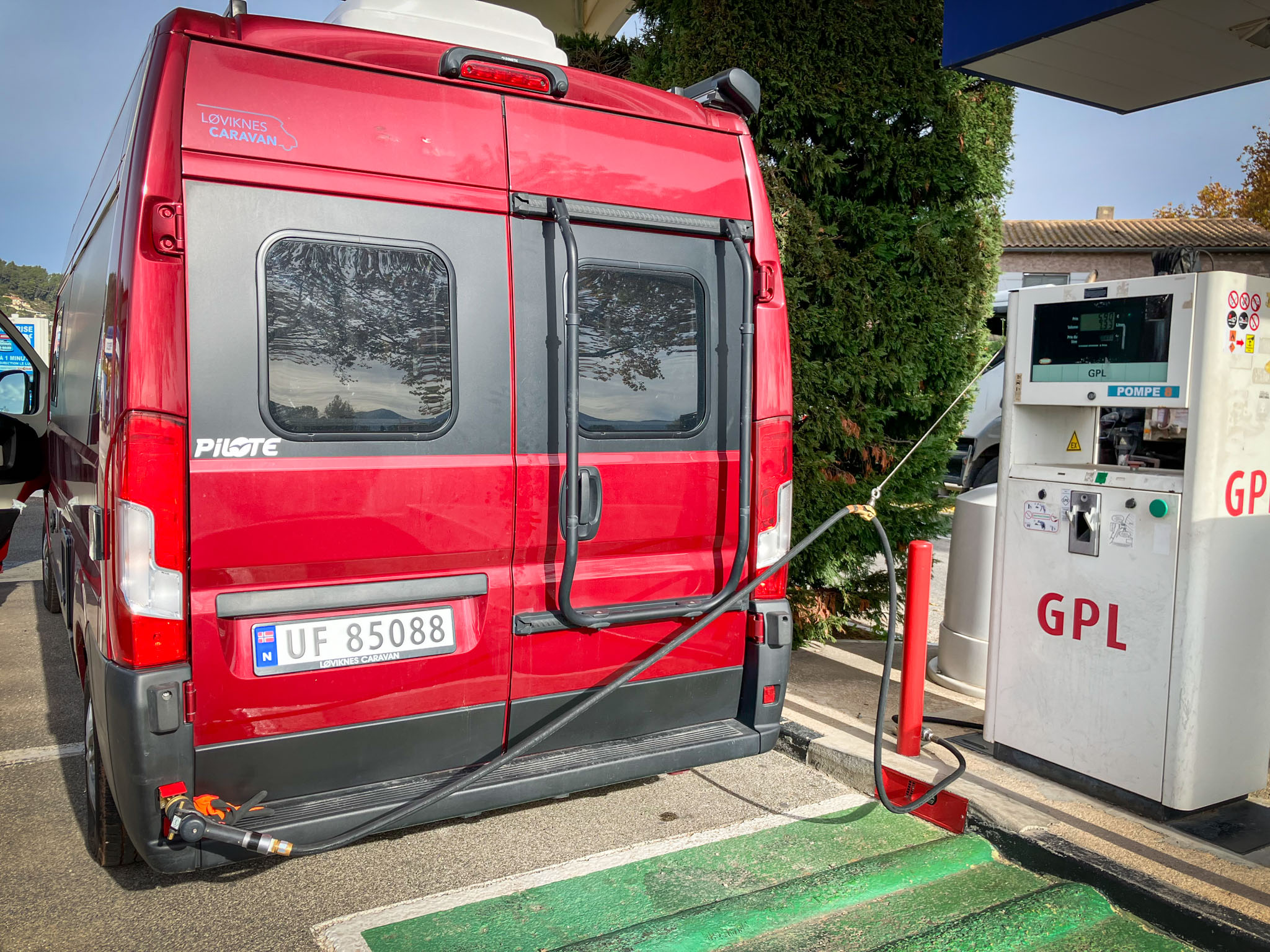 Bildet viser baksiden av en rød campervan som er koblet til gasstank for fylling