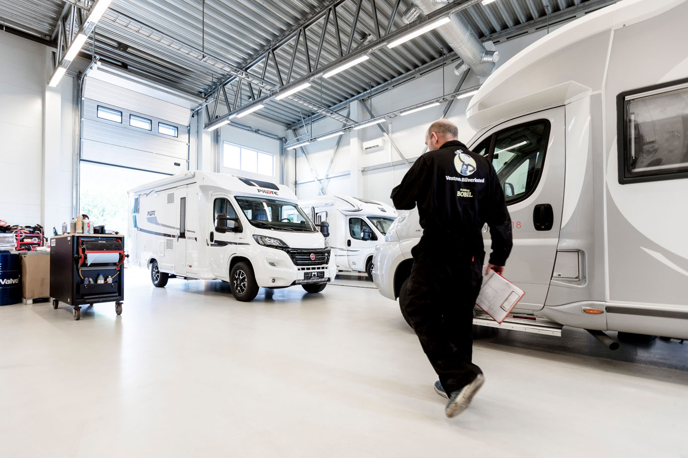 Innsiden av Vestnes Bilverksted. En mekaniker rusler forbi to bobiler